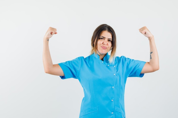 Vrouwelijke arts in blauw uniform die winnaargebaar toont en er gelukkig uitziet