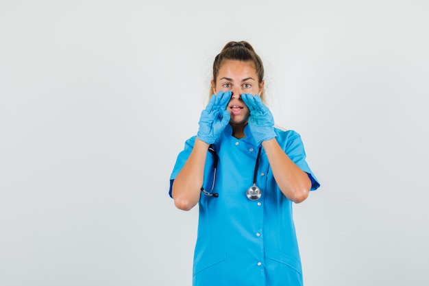 Vrouwelijke arts in blauw uniform, handschoenen die iets vertrouwelijks vertellen en nieuwsgierig kijken