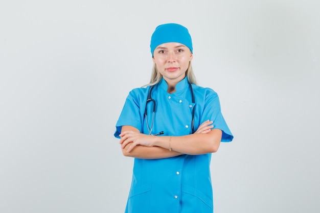 Vrouwelijke arts in blauw uniform lachend met gekruiste armen en hoopvol op zoek