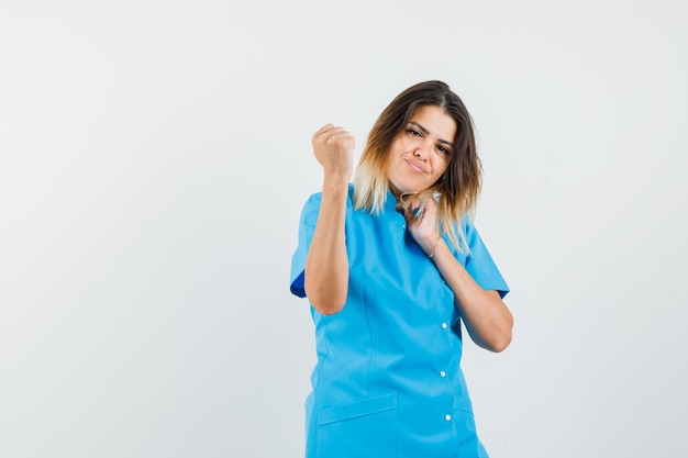 Vrouwelijke arts in blauw uniform met opgeheven vuist en zelfverzekerd?