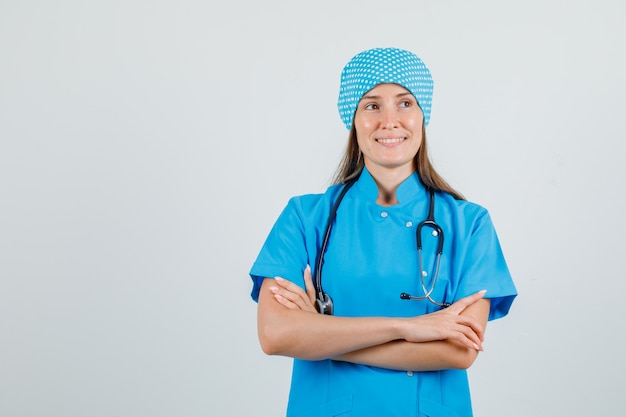 Vrouwelijke arts in blauw uniform wegkijken met gekruiste armen en hoopvol op zoek