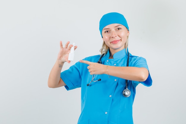 Vrouwelijke arts in blauw uniform wijzende vinger op medische fles en op zoek vrolijk