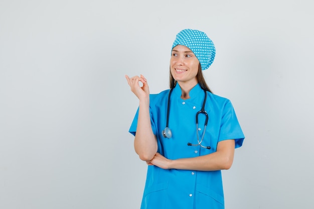 Vrouwelijke arts in blauw uniform wijzende vinger weg en op zoek blij