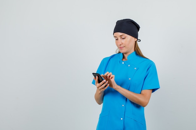 Vrouwelijke arts in blauw uniform, zwarte hoed met behulp van smartphone en bezig op zoek
