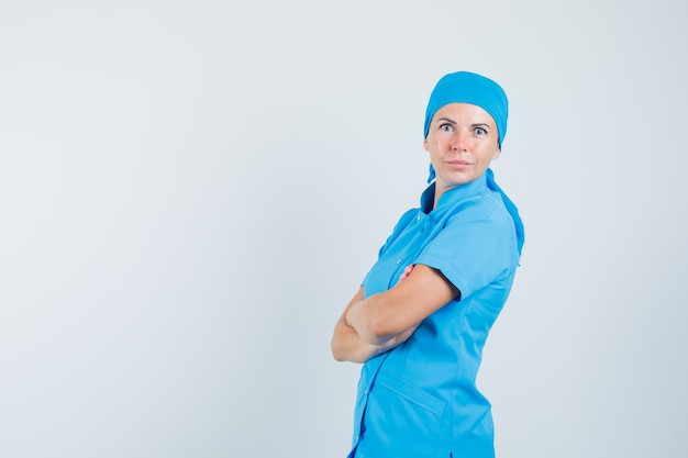 Vrouwelijke arts in blauwe uniforme staande met gekruiste armen en op zoek zelfverzekerd.