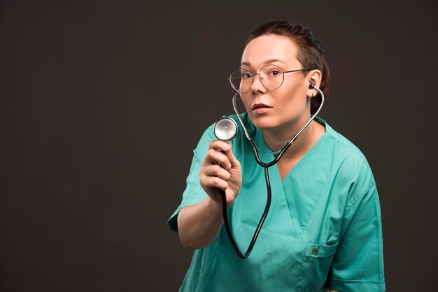 Vrouwelijke arts in groen uniform die een stethoscoop houdt en de patiënt luistert.