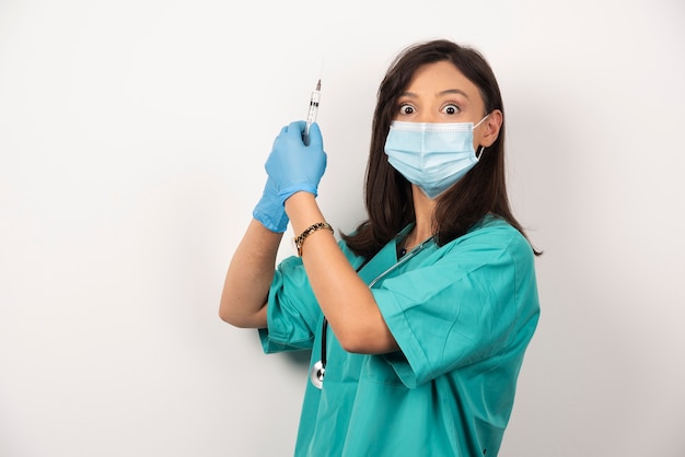 Vrouwelijke arts in medisch masker en handschoenen die spuit op witte achtergrond houden. Hoge kwaliteit foto