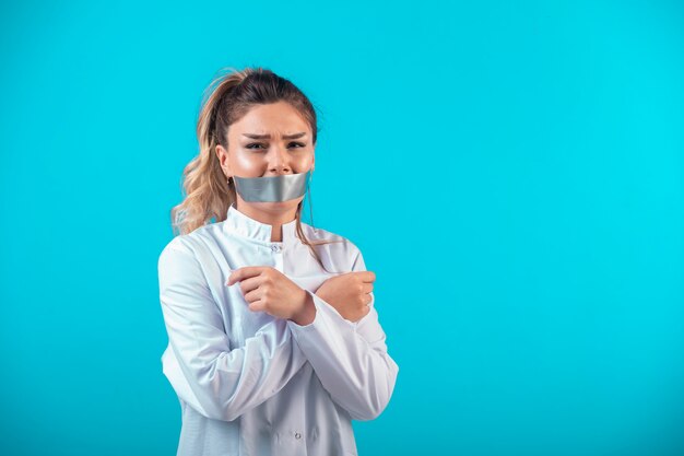 Vrouwelijke arts in wit uniform die haar mond bedekt en haar armen kruist