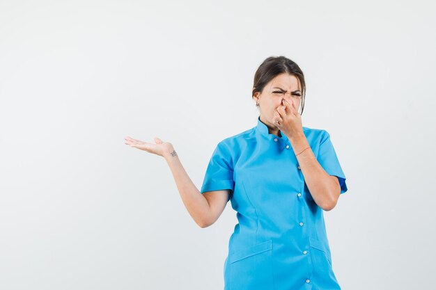 Vrouwelijke arts knijpt neus door slechte geur in blauw uniform en ziet er walgelijk uit