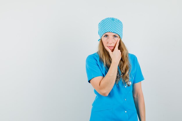 Vrouwelijke arts permanent denken pose in blauw uniform en op zoek verstandig.