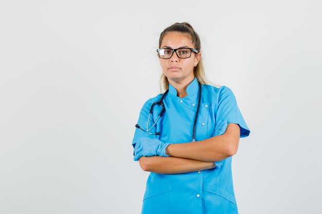 Vrouwelijke arts permanent met gekruiste armen in blauw uniform