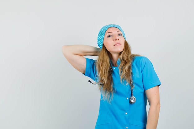 Vrouwelijke arts poseren met hand op nek in blauw uniform en op zoek zelfverzekerd.