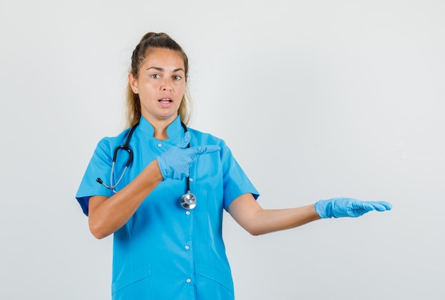 Vrouwelijke arts wijst naar kant met palm opzij gespreid in blauw uniform