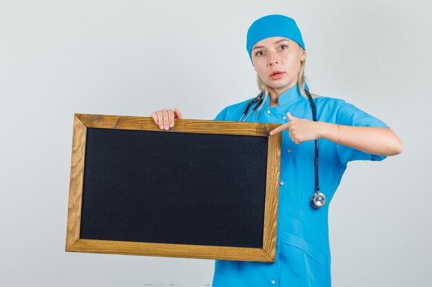 Vrouwelijke arts wijzende vinger op bord in blauw uniform en op zoek naar ernstig.