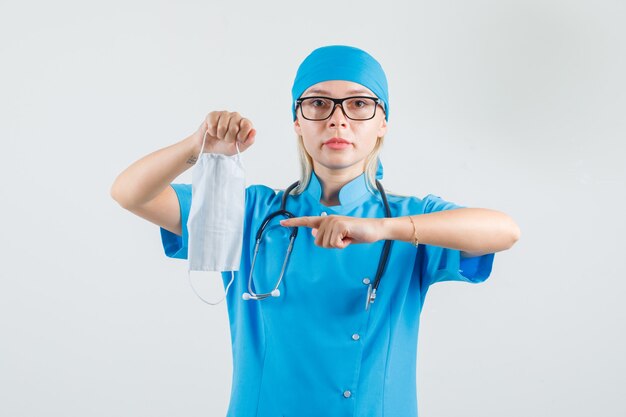 Vrouwelijke arts wijzende vinger op medisch masker in blauw uniform