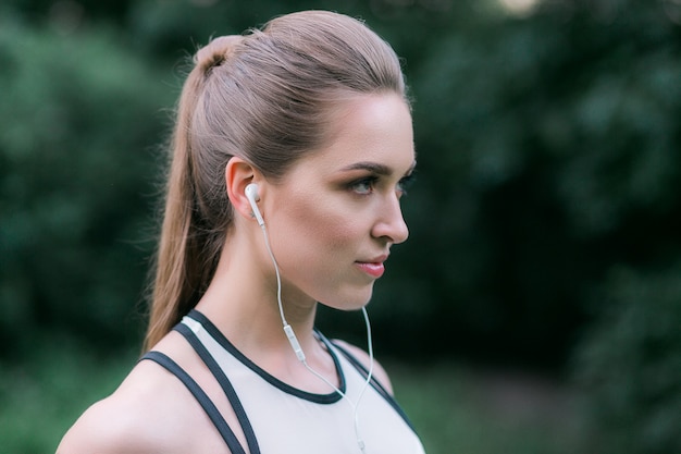 Vrouwelijke atleet die oortelefoons draagt. Vrouw die aan muziek luistert tijdens training openlucht.