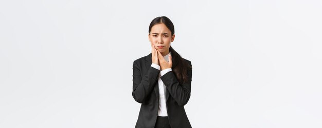Vrouwelijke Aziatische officemanager in zwart pak met kiespijn op het werk Onrustige zakenvrouw die hand op de wang houdt als pijn in de tanden moet een afspraak met een arts hebben die op een witte achtergrond staat