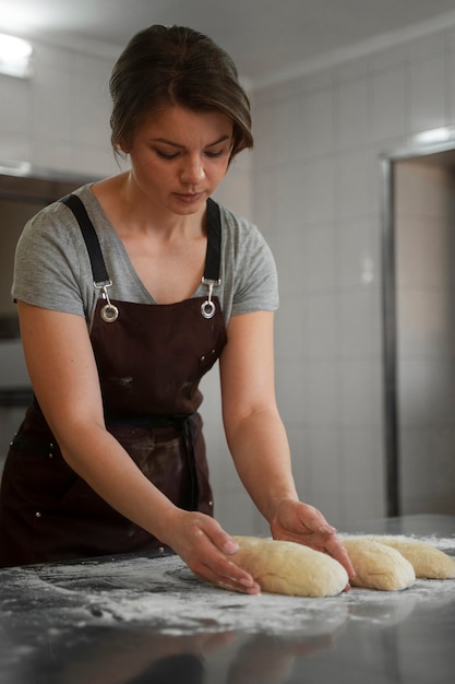 Gratis foto vrouwelijke bakker die brooddeeg hanteert in de banketbakkerij