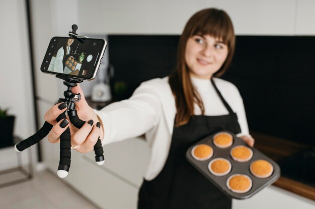 Vrouwelijke blogger die zichzelf opneemt met smartphone tijdens het bereiden van muffins