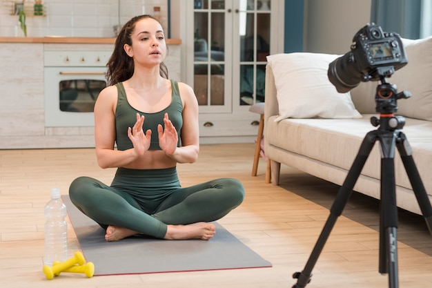 Vrouwelijke blogger in sportkleding zittend op yoga mat