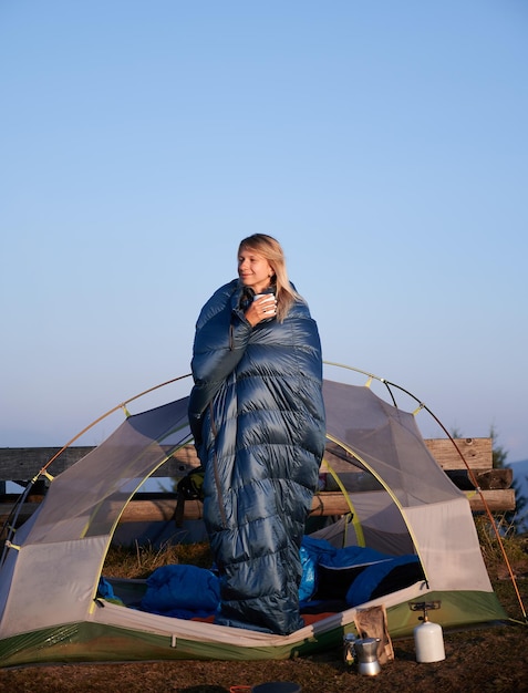 Vrouwelijke blonde rust in tent gewikkeld in slaapzak buitenshuis