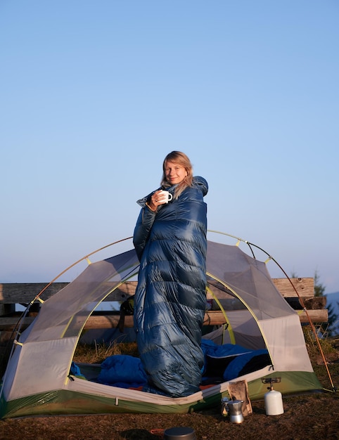 Vrouwelijke blonde rust in tent gewikkeld in slaapzak buitenshuis