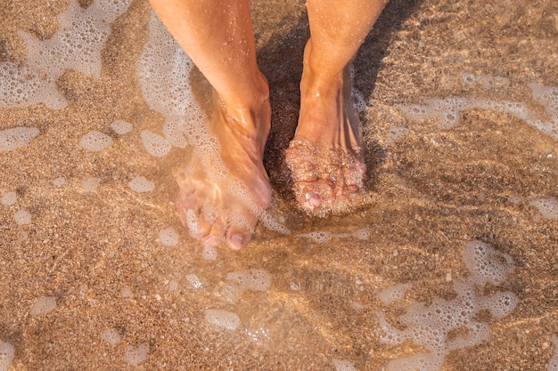 Vrouwelijke blote voeten staan in de zee op een zandstrand. bovenaanzicht, plat gelegd. Premium Foto