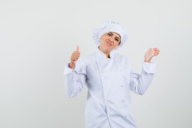 Vrouwelijke chef-kok die duim in wit uniform toont en vrolijk kijkt