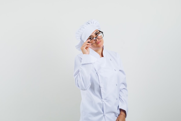 Vrouwelijke chef-kok die glazen in wit uniform opstijgt en er verstandig uitziet