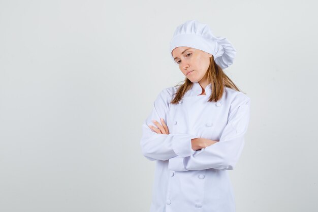 Vrouwelijke chef-kok die zich met gekruiste wapens in wit uniform bevindt en peinzend kijkt. vooraanzicht.