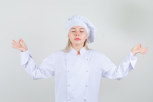 Vrouwelijke chef-kok doet meditatie met gesloten ogen in wit uniform en kijkt ontspannen.