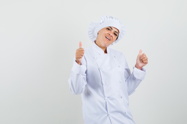 Vrouwelijke chef-kok dubbele duimen opdagen in wit uniform en op zoek zelfverzekerd