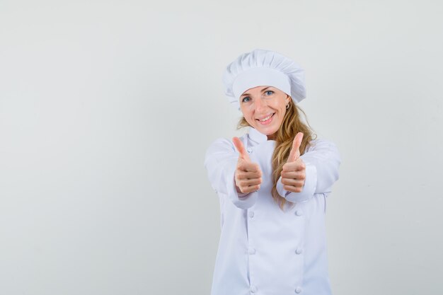 Vrouwelijke chef-kok dubbele duimen opdagen in wit uniform en vrolijk kijken