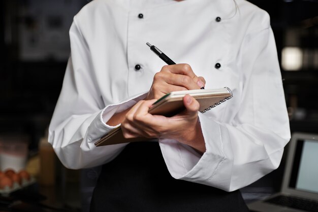 Vrouwelijke chef-kok in de keuken die aantekeningen maakt met pen en notitieboekje