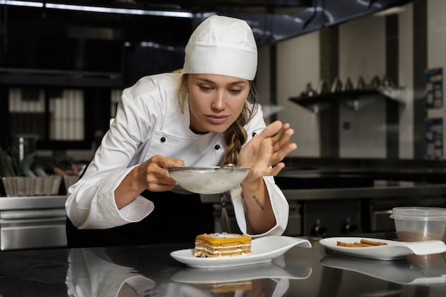 Gratis foto vrouwelijke chef-kok in de keuken die poedersuiker op dessert zeven