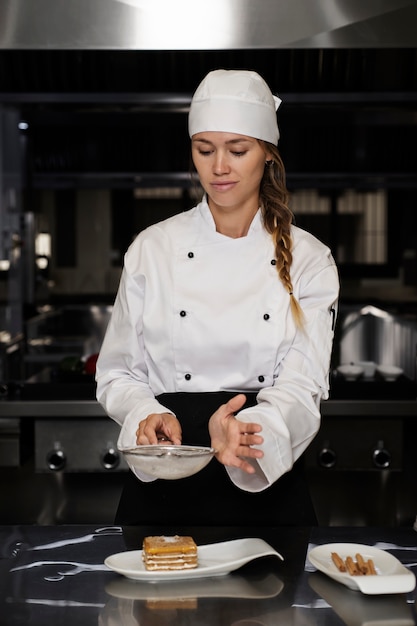 Vrouwelijke chef-kok in de keuken die poedersuiker op dessert zeven