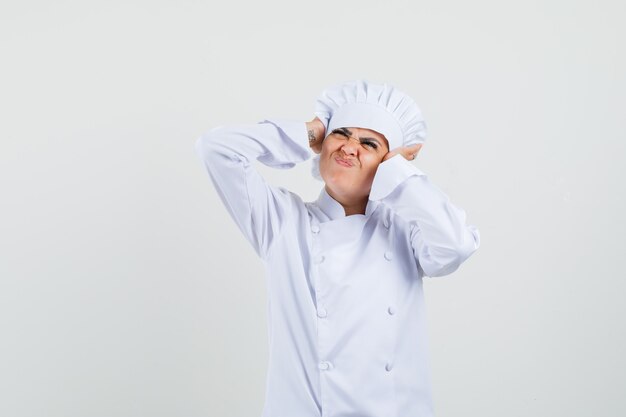 Vrouwelijke chef-kok in wit uniform hand in hand op oren en op zoek geïrriteerd