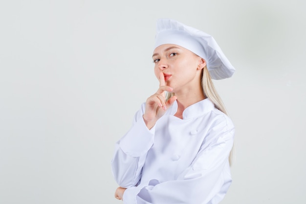 Vrouwelijke chef-kok in wit uniform stilte gebaar tonen en glimlachen