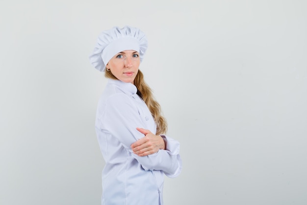 Vrouwelijke chef-kok in witte uniforme staande met gekruiste armen en op zoek zelfverzekerd.