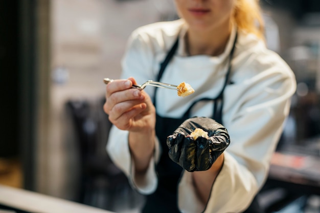 Vrouwelijke chef-kok met handschoen die voedsel test als het wordt gekookt