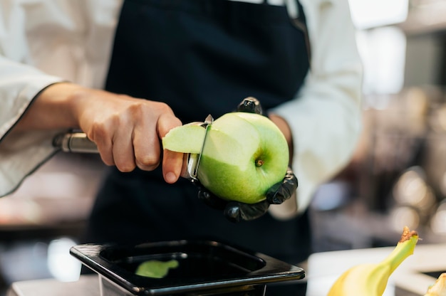 Vrouwelijke chef-kok met handschoen en schort die appelschil verwijderen