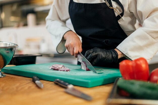 Vrouwelijke chef-kok met schort en handschoen hakkende groenten