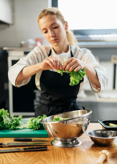 Vrouwelijke chef-kok met schort scheuren salade in kom