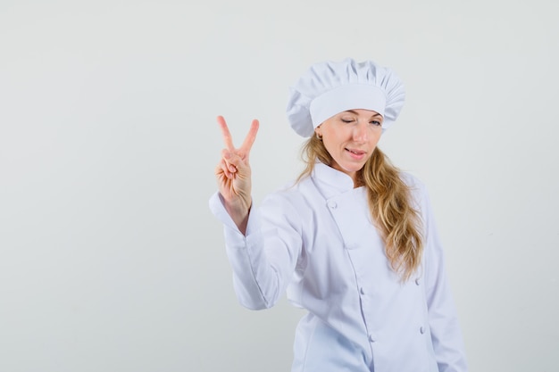 Vrouwelijke chef-kok met v-teken en knipogen oog in wit uniform