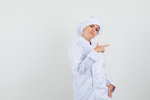 Vrouwelijke chef-kok wijst naar de kant in wit uniform en kijkt serieus.
