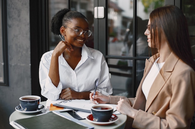 Vrouwelijke collega's bespreken gegevens in het café buiten. Multiraciale vrouwelijke personen die productieve strategie analyseren voor zakelijke projectie met behulp van documenten in straatcafé
