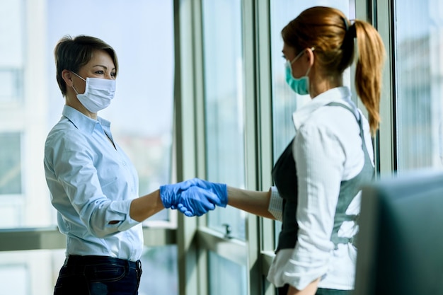 Vrouwelijke collega's die gezichtsmaskers en handschoenen dragen tijdens het begroeten op kantoor