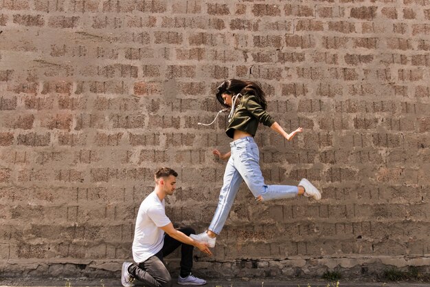 Vrouwelijke danser die op man hand tegen steenmuur springt