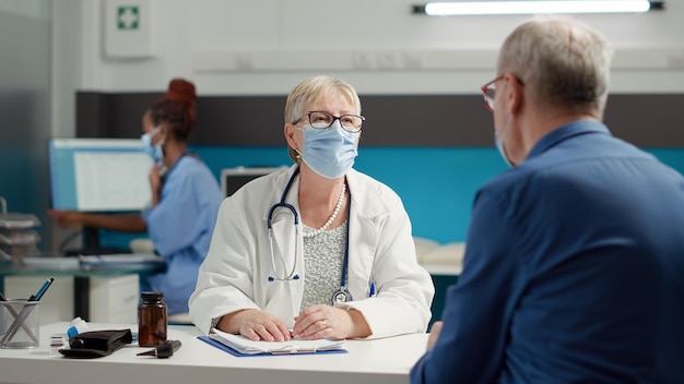 Vrouwelijke dokter die gepensioneerde zieke patiënt in medische kast raadpleegt, die een onderzoeksafspraak bijwoont in het gezondheidscentrum. controlebezoek overleg met diagnose behandeling tijdens pandemie.