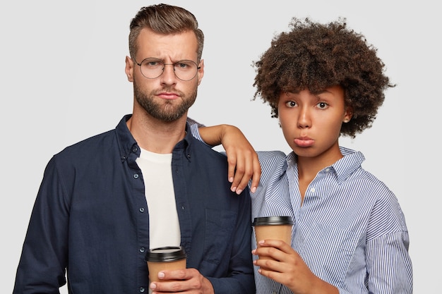 Gratis foto vrouwelijke en mannelijke studenten van gemengd ras hebben ontevreden uitdrukkingen, drinken koffie na colleges, ontevreden over examenresultaten. afro-amerikaanse vrouw leunt naar de schouder van metgezel, staan samen